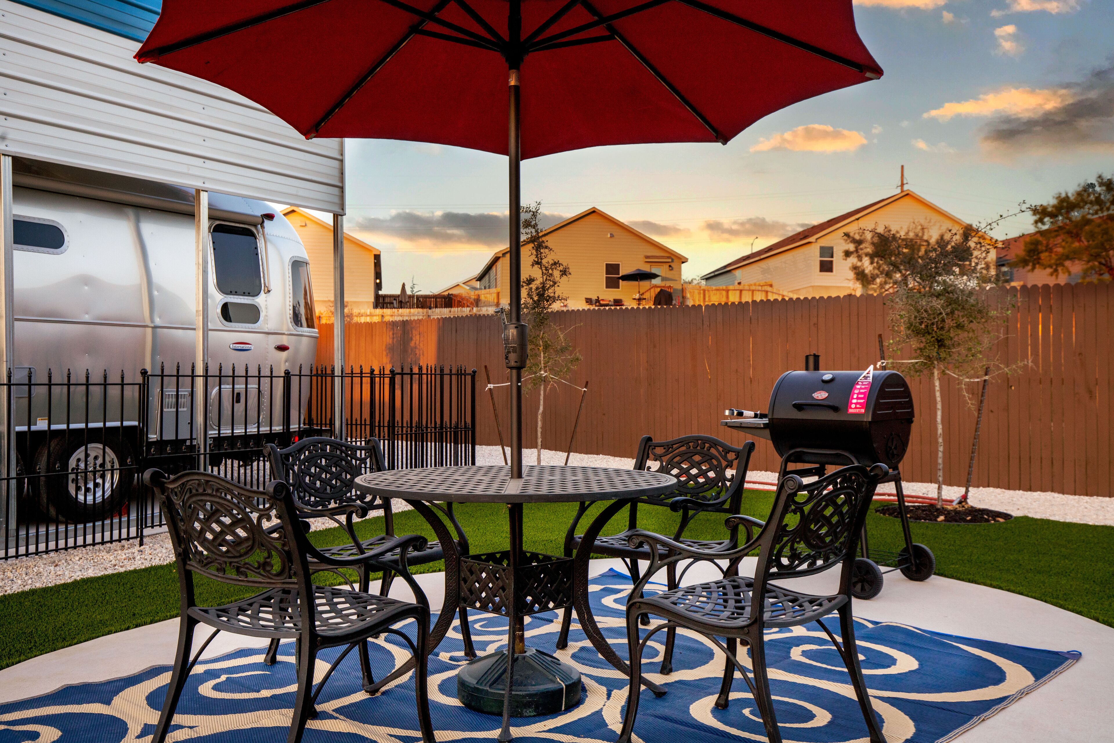 Une terrasse avec une table ronde et des chaises, un barbecue et un parasol rouge.