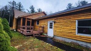 A log cabin with a wooden deck, a front door, and a window.