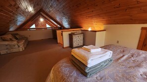 A cozy attic bedroom with a sloped ceiling, a bed with a patterned bedspread, a small wooden cabinet, and a sofa with floral upholstery.