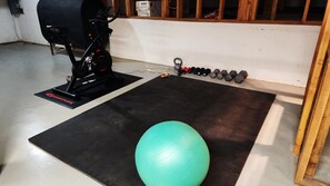 A gym with a stationary bike, a green exercise ball, and a set of dumbbells.