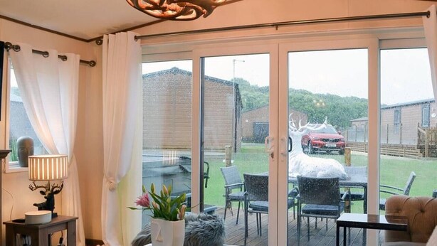 Sala de estar con sofá, mesa de centro y lámpara. Hay una puerta corrediza de vidrio que da a un patio exterior con sillas y una parrilla.