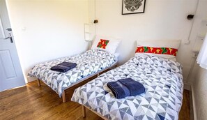 Two single beds with geometric patterned bedding, a white wall, and a door.