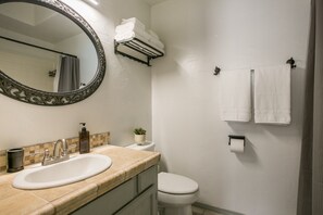 Une salle de bain avec un lavabo, des toilettes et un miroir. Des serviettes sont accrochées au mur et une petite plante est posée sur le comptoir.