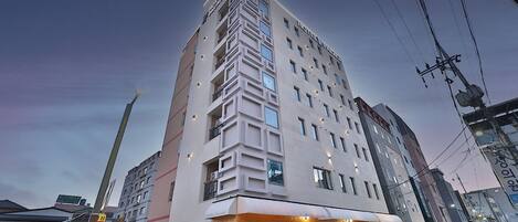 Et hotel i flere etager med moderne arkitektur, der har en markant indgang med et rundt vindue og et skilt, der angiver, at det er et hotel.