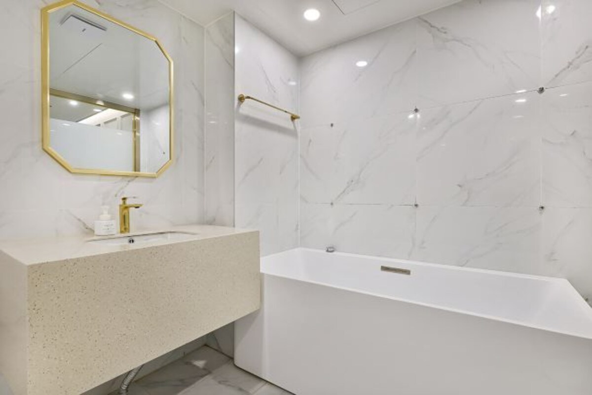 Un baño moderno con una bañera independiente, un espejo grande con marco dorado y una pared de mármol.
