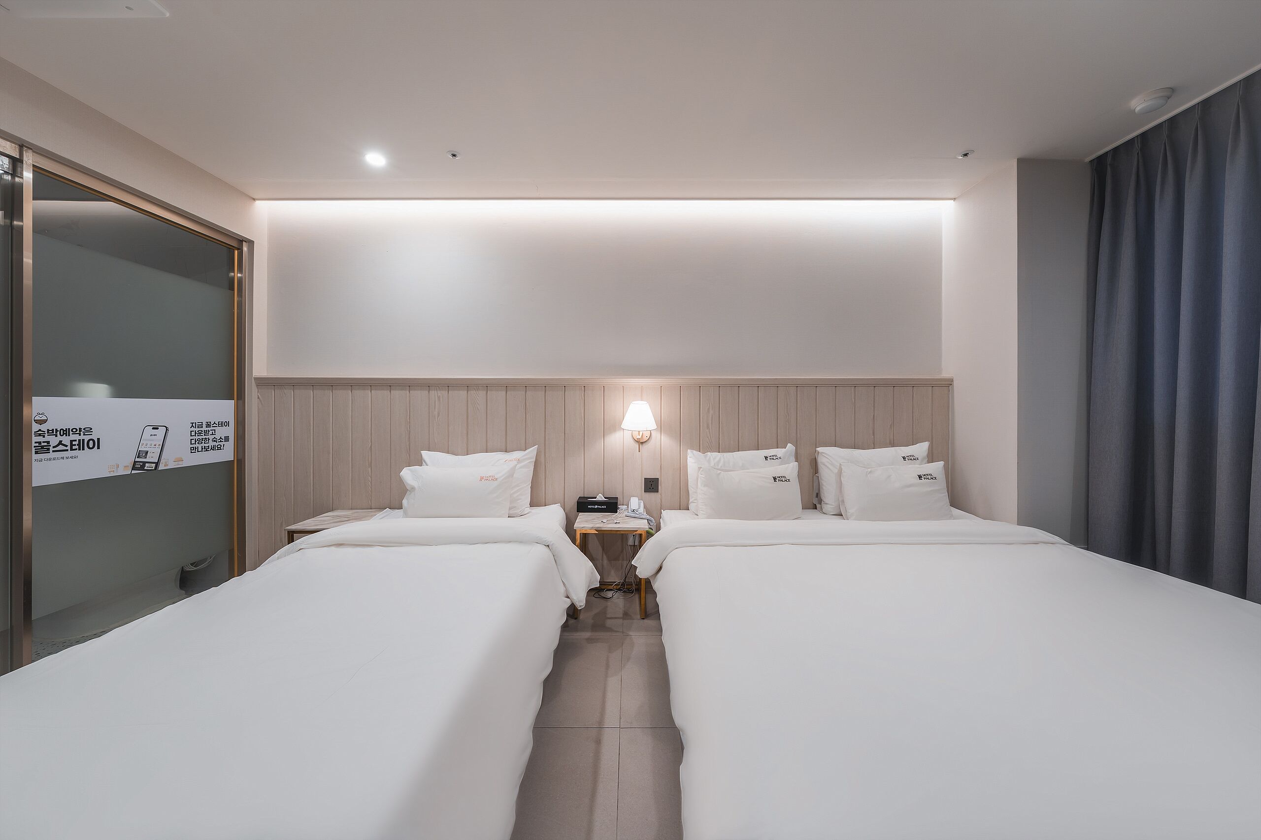 Ein Hotelzimmer mit zwei Betten, einem Nachttisch mit Lampe, einem Telefon und einer Wandleuchte.