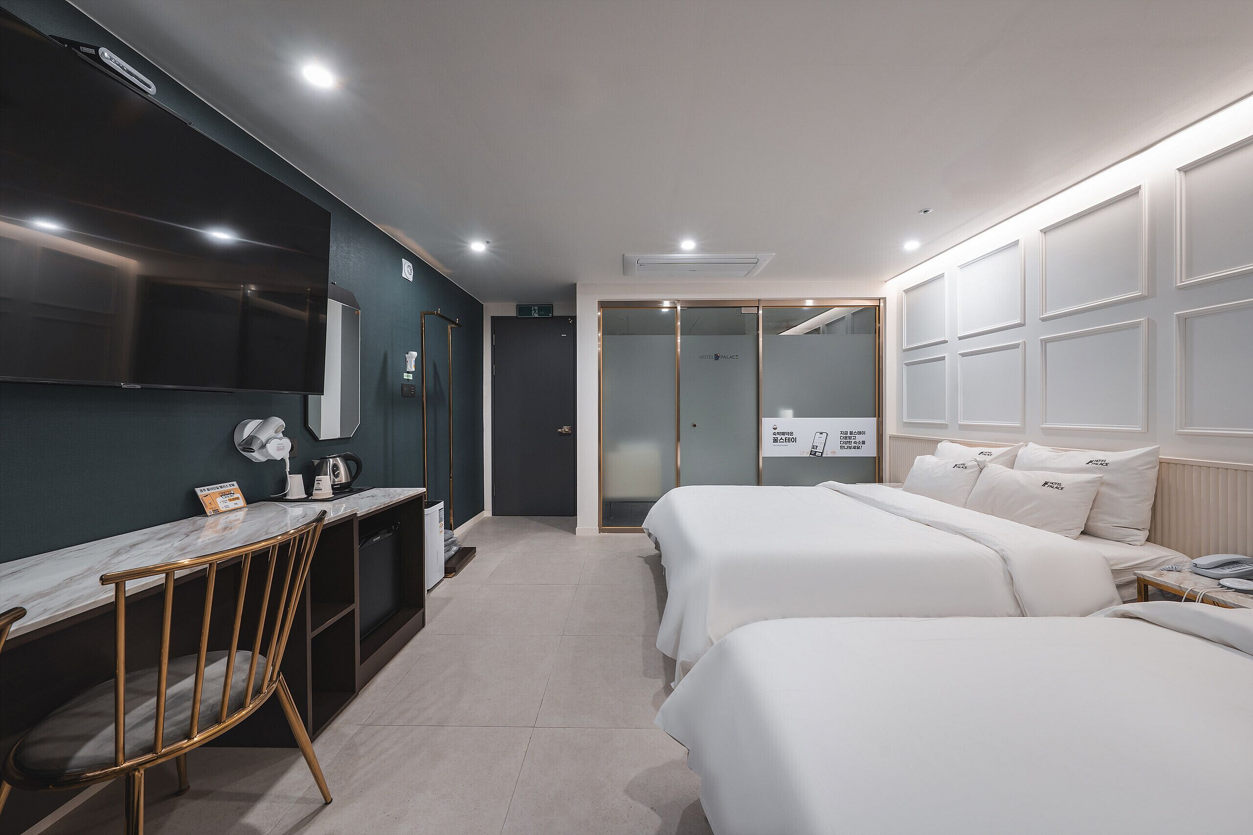 Une chambre d’hôtel équipée d’un bureau, de deux lits, d’un miroir, d’une armoire et d’un espace douche.