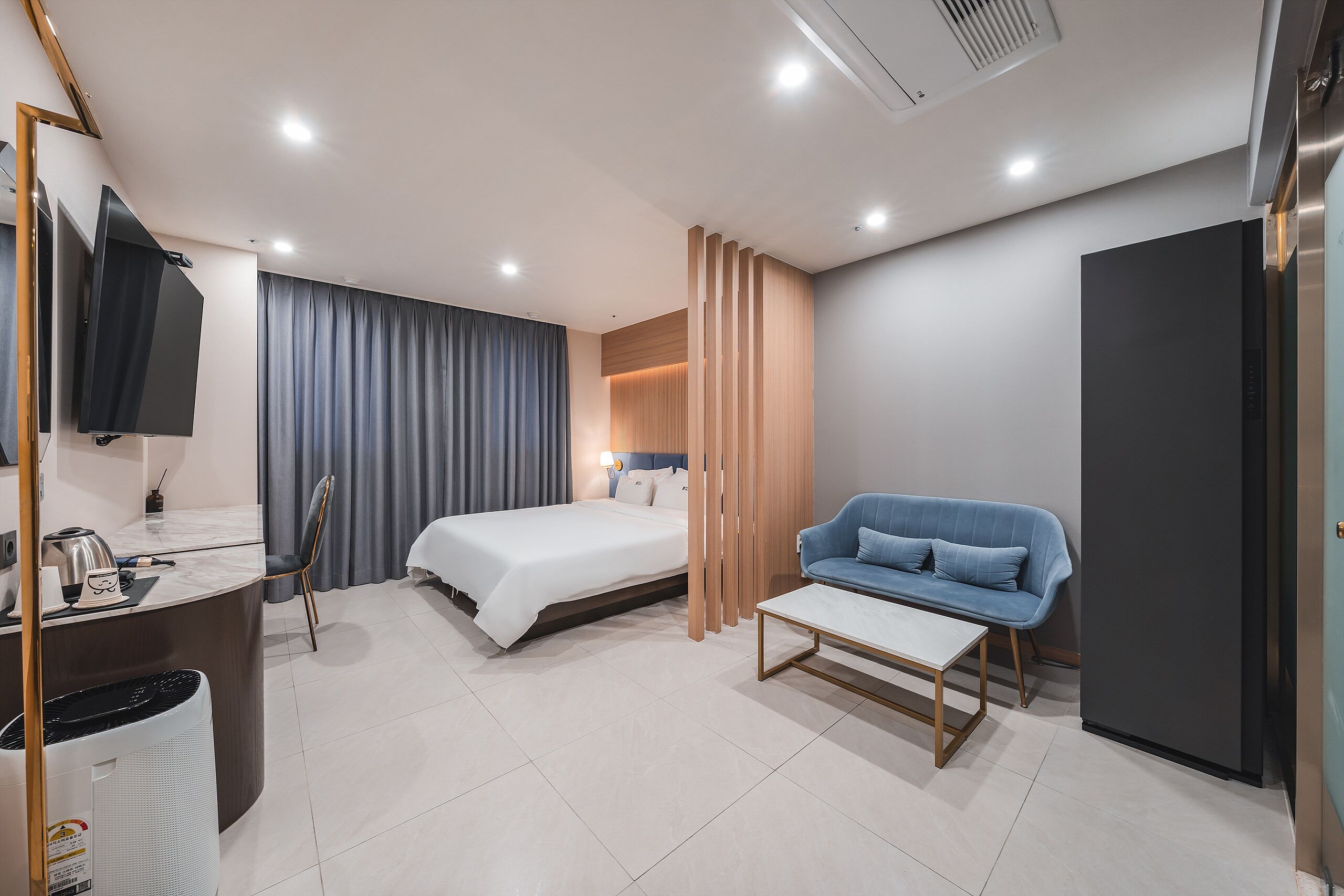 A modern hotel room with a bed, a sofa, a desk, a TV, and a minibar.