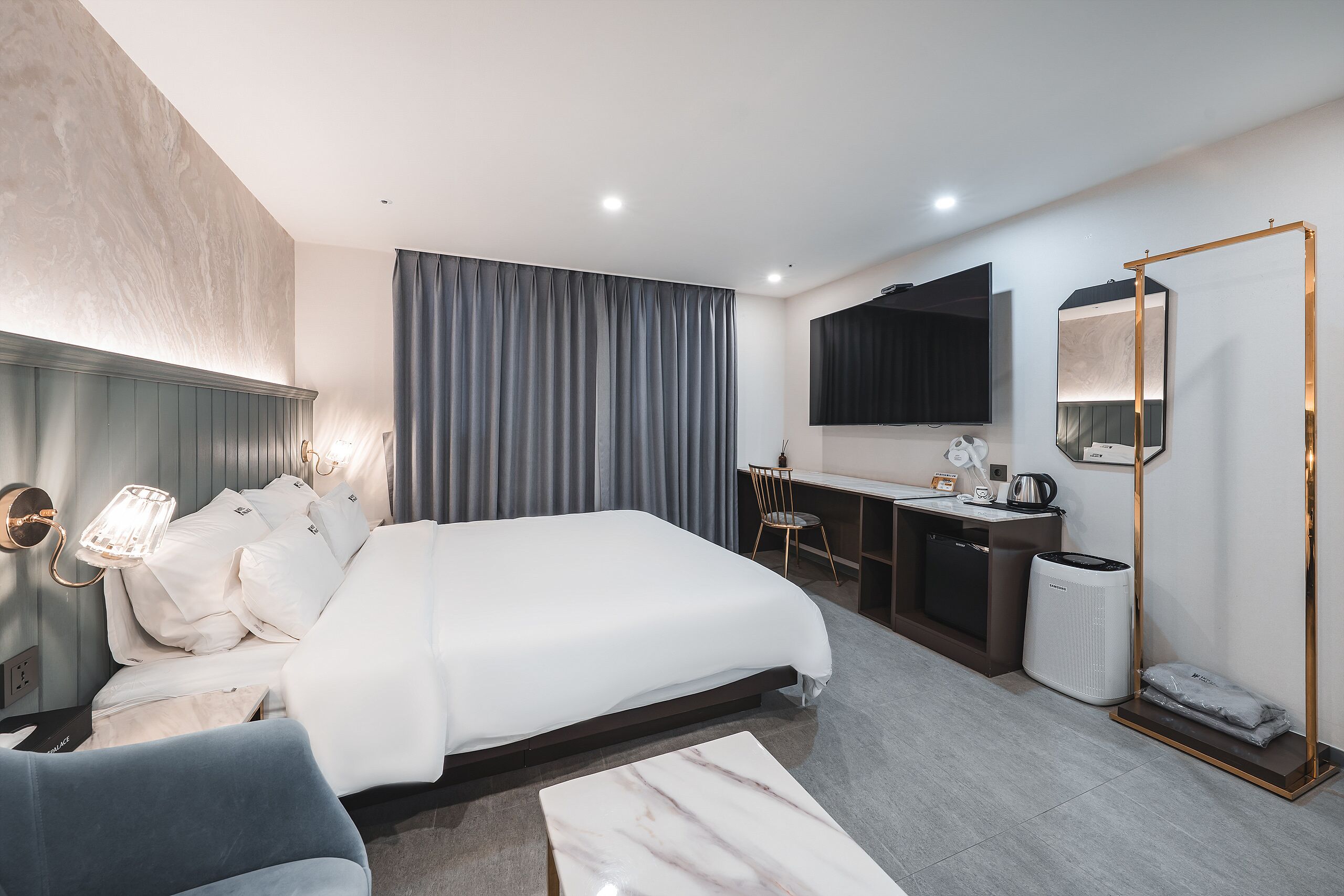 A modern hotel room with a large bed, bedside table, lamp, desk, chair, and a mirror.