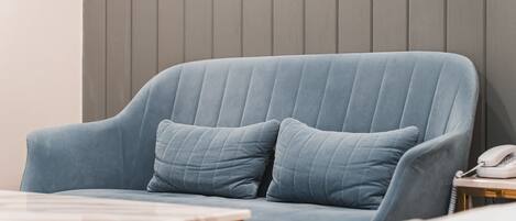 Un sofá azul con dos cojines, una mesita de madera con un teléfono blanco y una mesa con cubierta de mármol.
