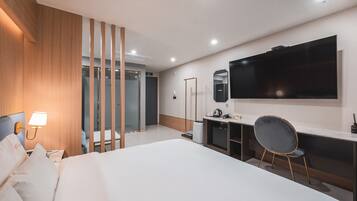 A modern hotel room with a large bed, a desk, a chair, a TV, and a mirror.