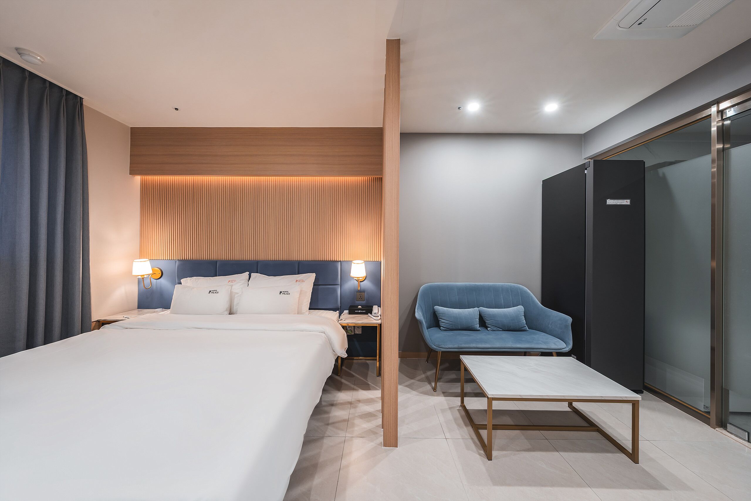 A modern hotel room with a large bed, a desk, a chair, and a wardrobe.