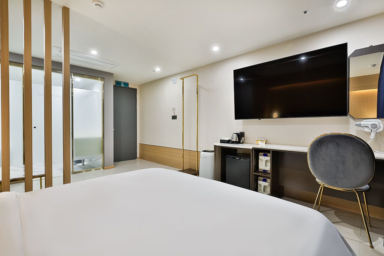 Une chambre d’hôtel moderne dotée d’un grand lit, d’un bureau avec une chaise, d’un téléviseur à écran plat, d’un miroir et d’un espace douche.