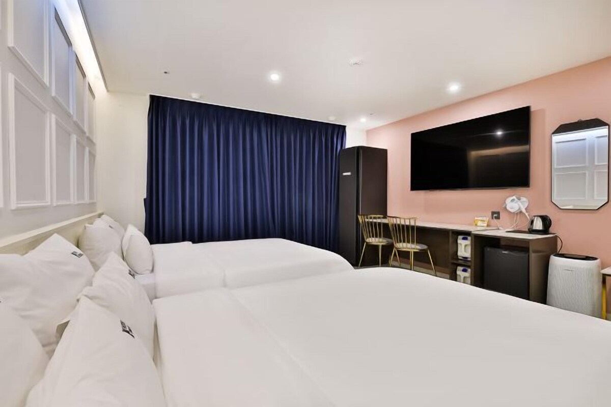 Habitación de hotel con dos camas, un escritorio, un televisor y un espejo.