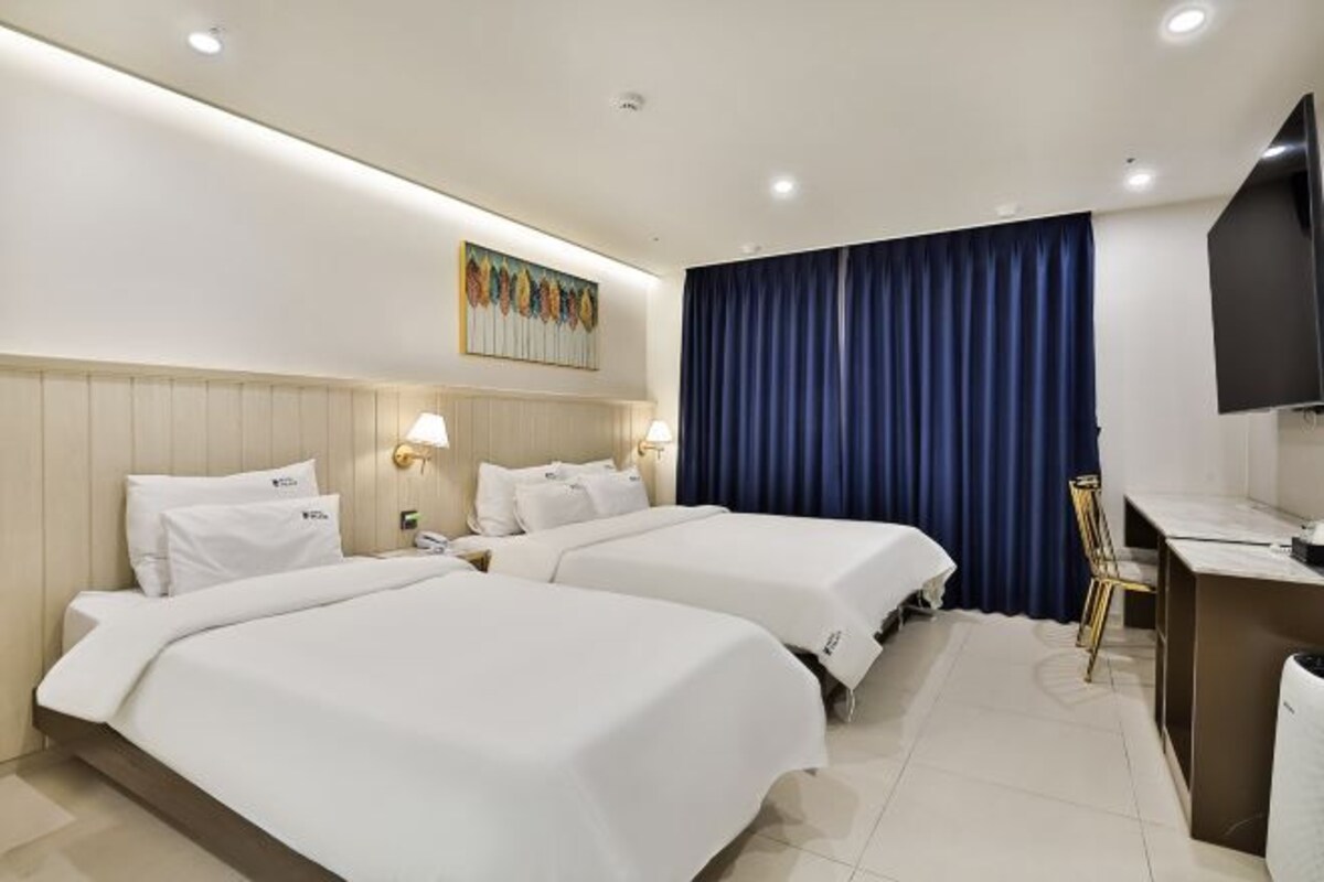 Habitación de hotel con dos camas, un escritorio, una silla, un televisor y un cuadro en la pared.