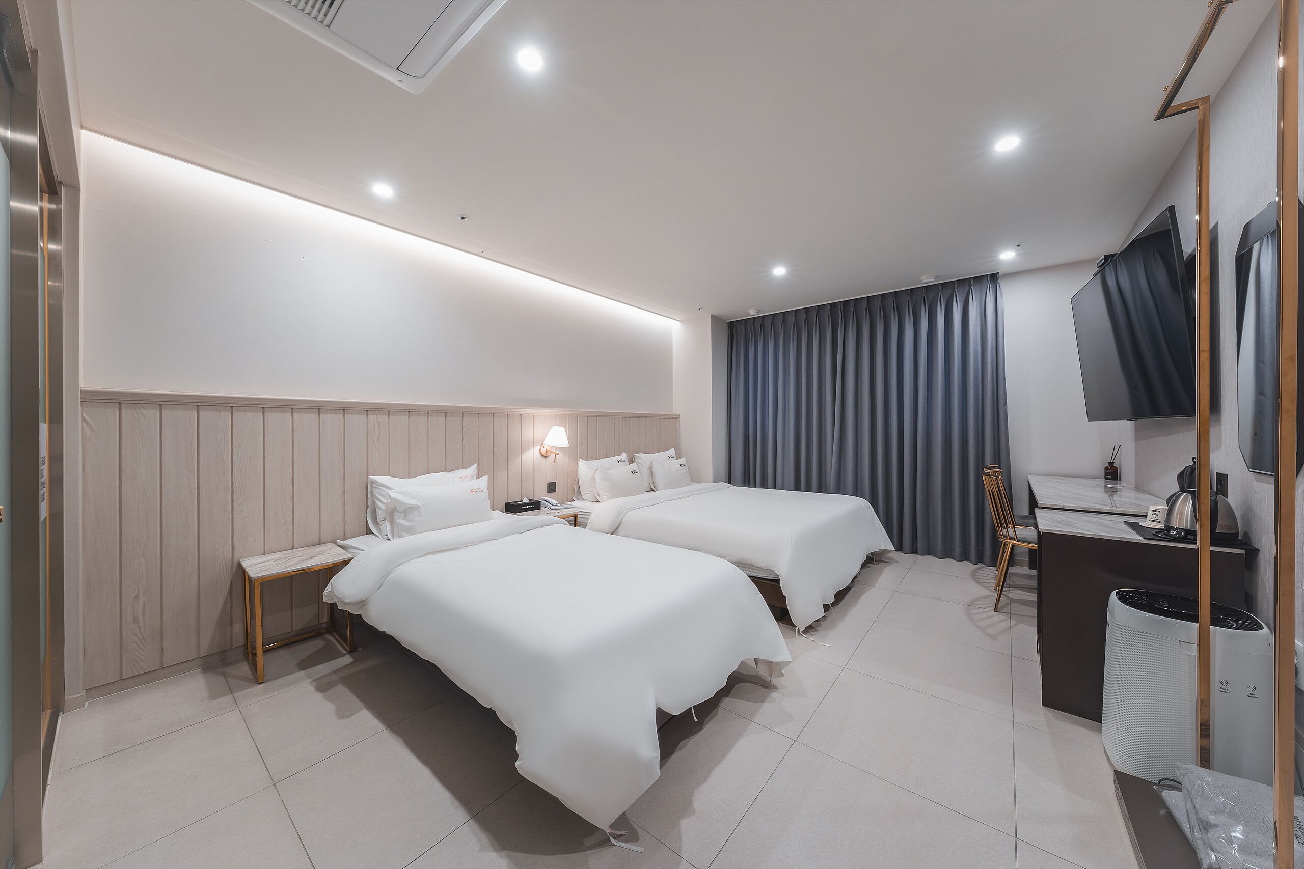 A modern hotel room with two beds, a desk, a chair, a TV, and a large window with curtains.