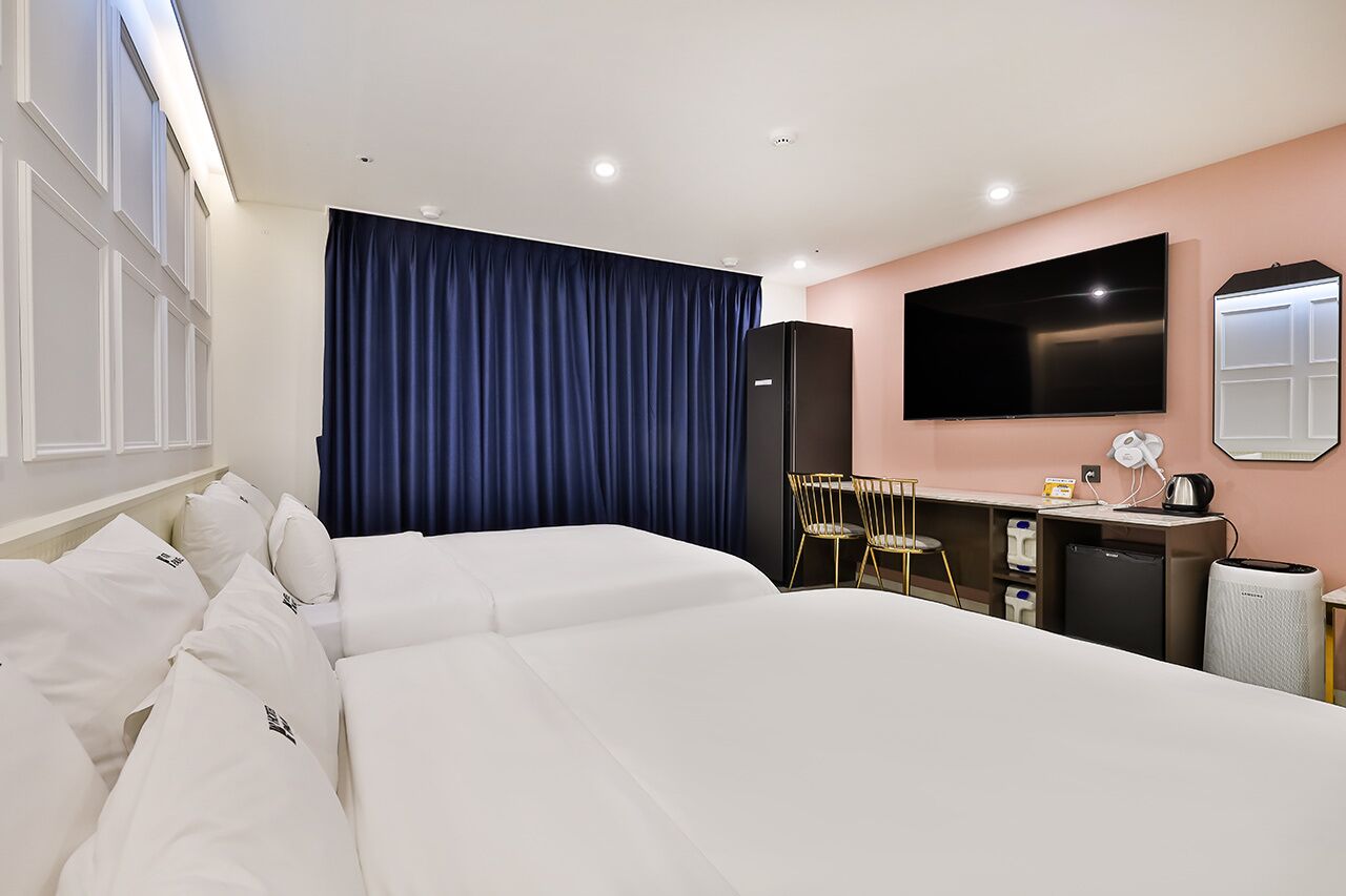 Quarto de hotel com uma cama grande, uma escrivaninha com cadeira, televisão de tela plana, espelho e uma pequena cozinha.