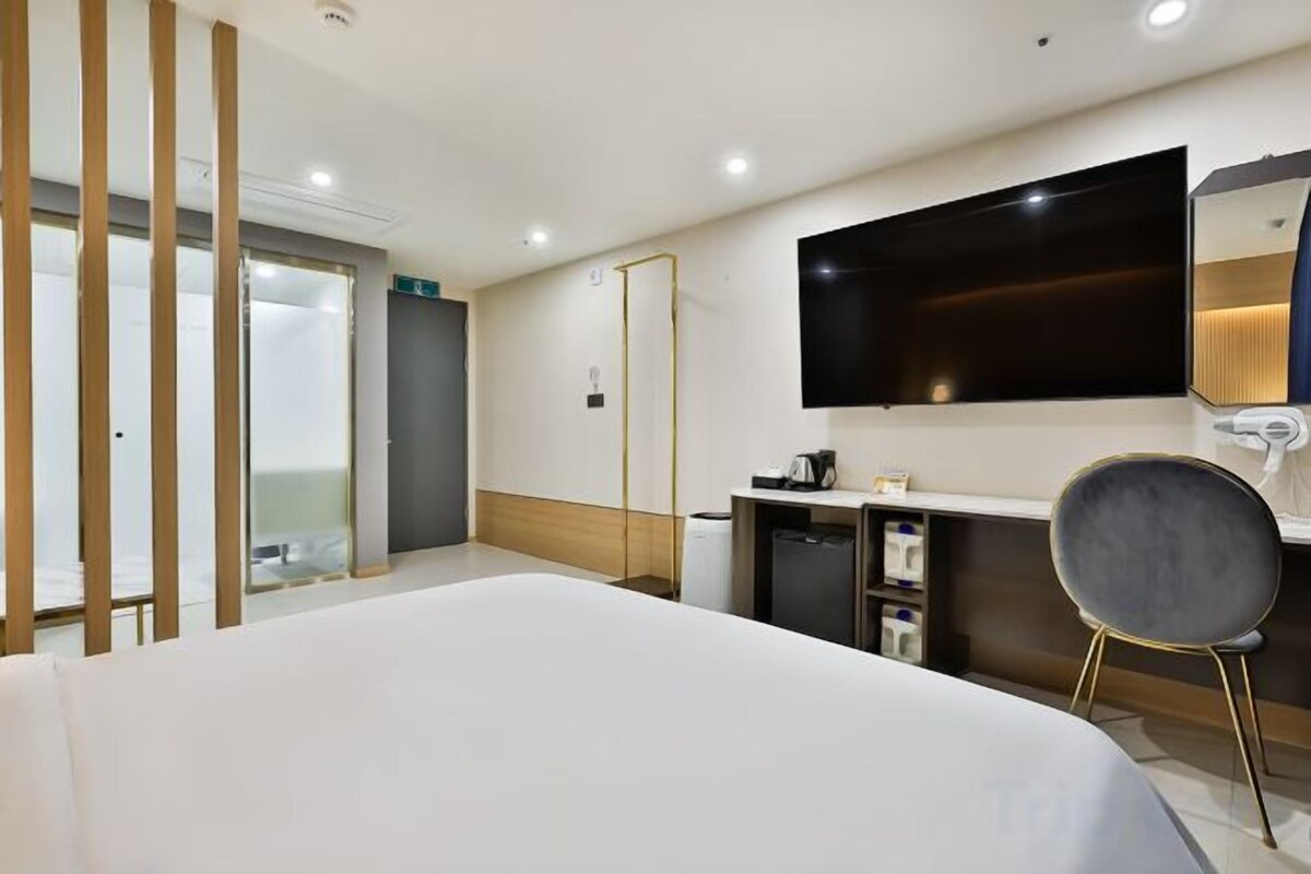 A hotel room with a bed, a desk, a chair, a TV, and a mirror.