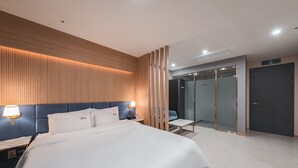 A modern hotel room with a large bed, a bedside table with a lamp, a glass-enclosed shower area, and a dark door. - Hotel Palace Gyeongju (Gyeongju)
