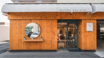 A hotel entrance with a wooden facade, a circular mirror, and a sign reading "HOTEL PALACE".