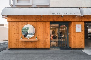 A hotel entrance with a wooden facade, a circular mirror, and a sign reading "HOTEL PALACE".