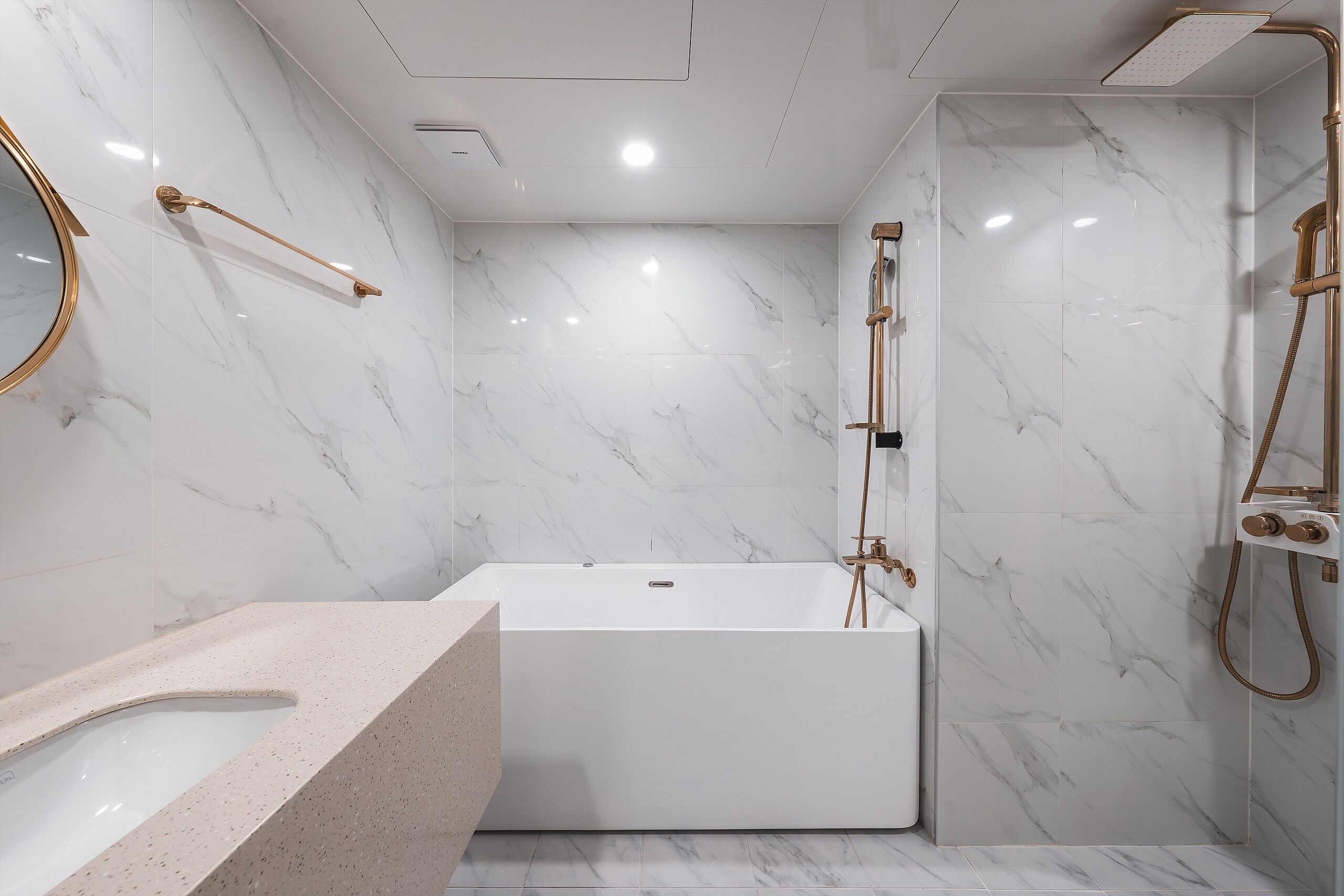 A modern bathroom with a marble wall, a freestanding bathtub, a gold showerhead, and a round mirror.
