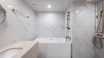 A modern bathroom with a marble wall, a freestanding bathtub, a gold showerhead, and a round mirror.