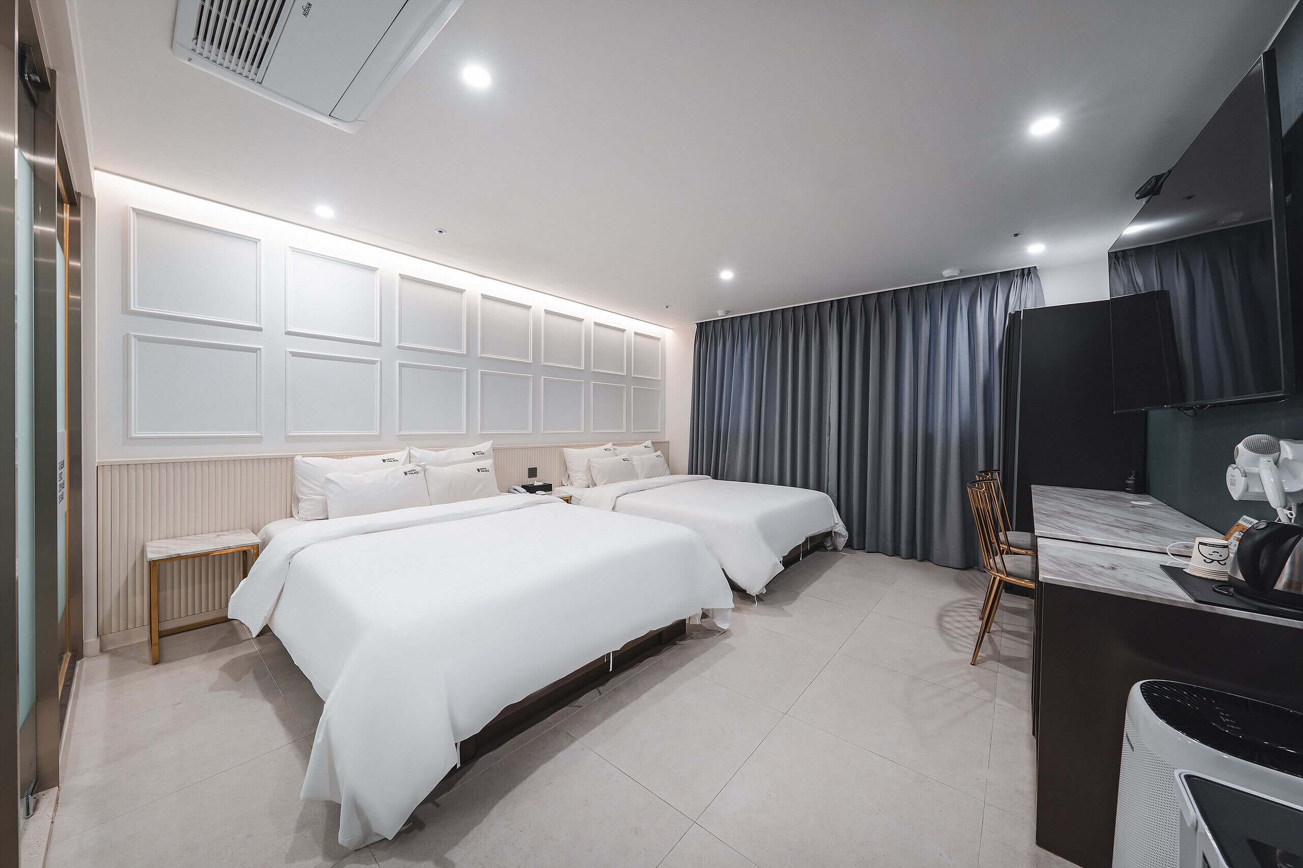 A hotel room with two beds, a desk, a chair, a television, and a radiator.
