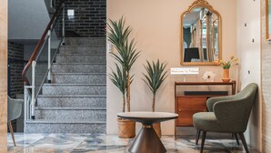A staircase with a wooden handrail, a marble floor, a round table with a wooden base, two potted plants, a green upholstered chair, and a mirror with a gold frame. - Hotel Palace Gyeongju (Gyeongju)