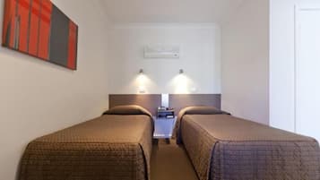 A hotel room with two single beds, a small bedside table, a nightstand, and a wall-mounted air conditioning unit.