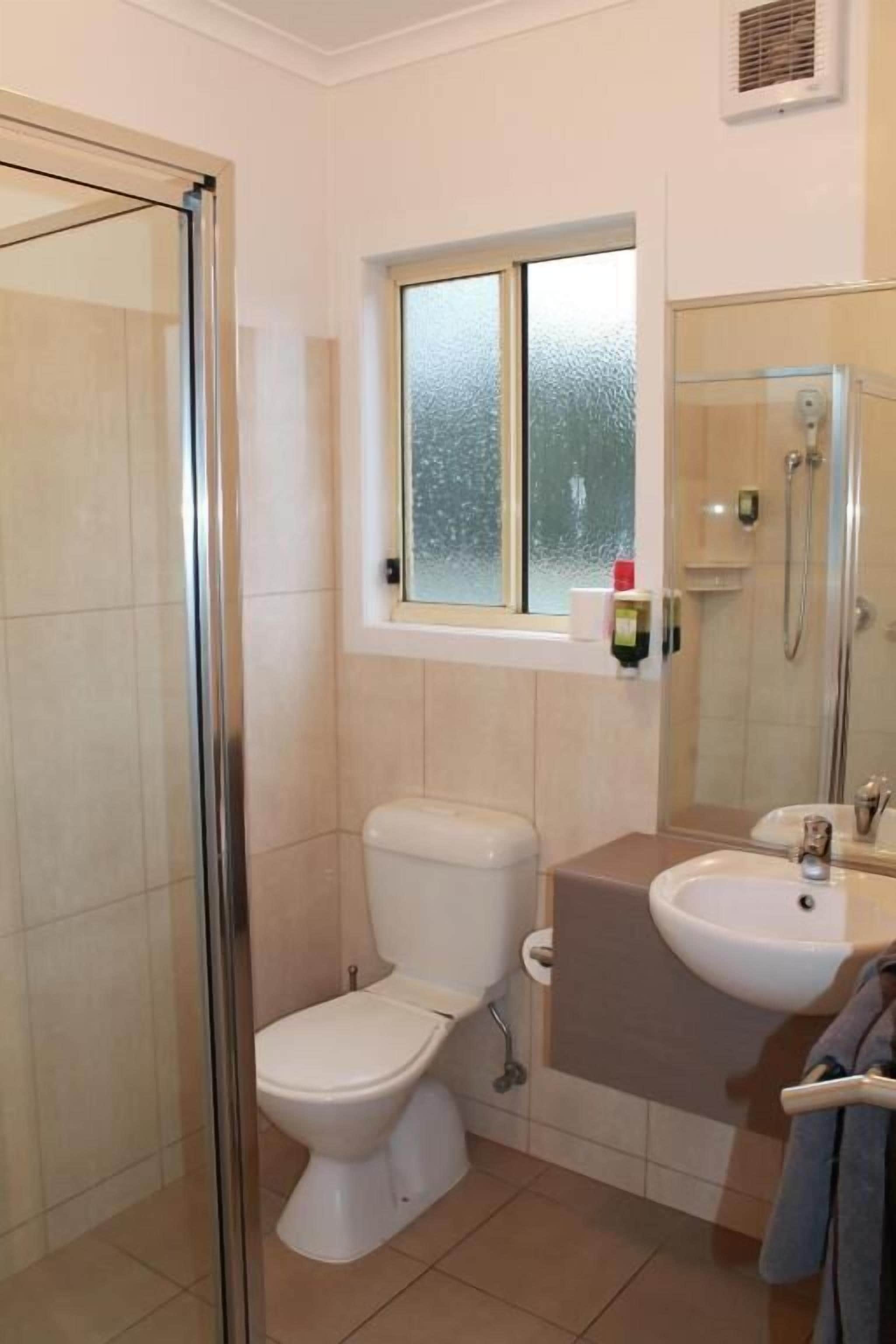 A bathroom with a glass shower enclosure, a toilet, a sink, and a window above the toilet.