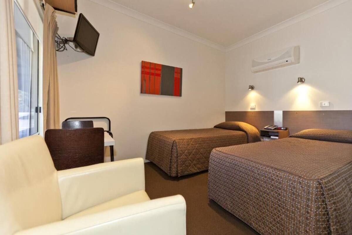 A hotel room with two beds, a sofa, a TV mounted on the wall, and a painting above the beds.