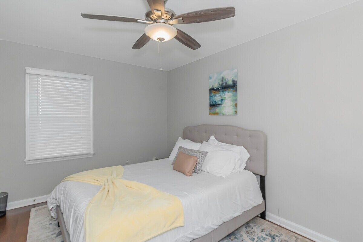 Ein Schlafzimmer mit einem Bett, einem Deckenventilator, einem Fenster mit Jalousien und einem Gemälde an der Wand.