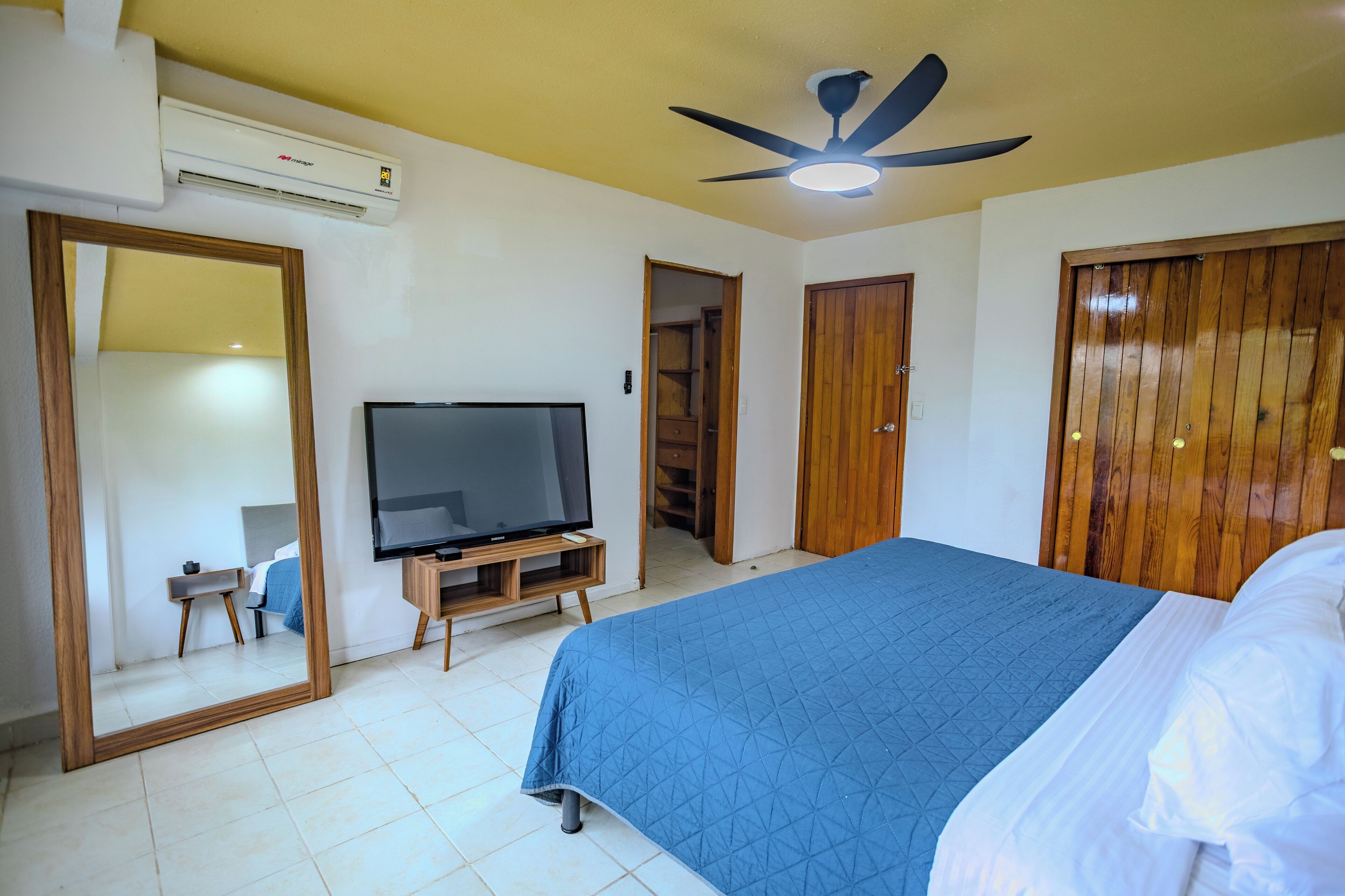 Quarto com uma cama, televisão em suporte de madeira, ventilador de teto e guarda-roupa.