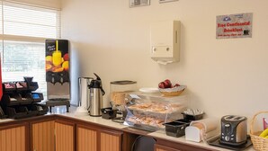 Una barra de desayuno con máquinas de café, dispensador de zumo de frutas y un cartel que indica desayuno continental gratuito.
