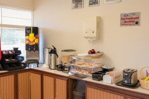 En morgenmadsbar med kaffemaskiner, en juice-dispenser og et skilt, der angiver gratis kontinental morgenmad.