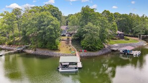 A lakeside property with a dock, a boat, and a house surrounded by trees. - Shoreside Oasis - Amazing Views & Spacious 5BR 4BA (Mooresville)