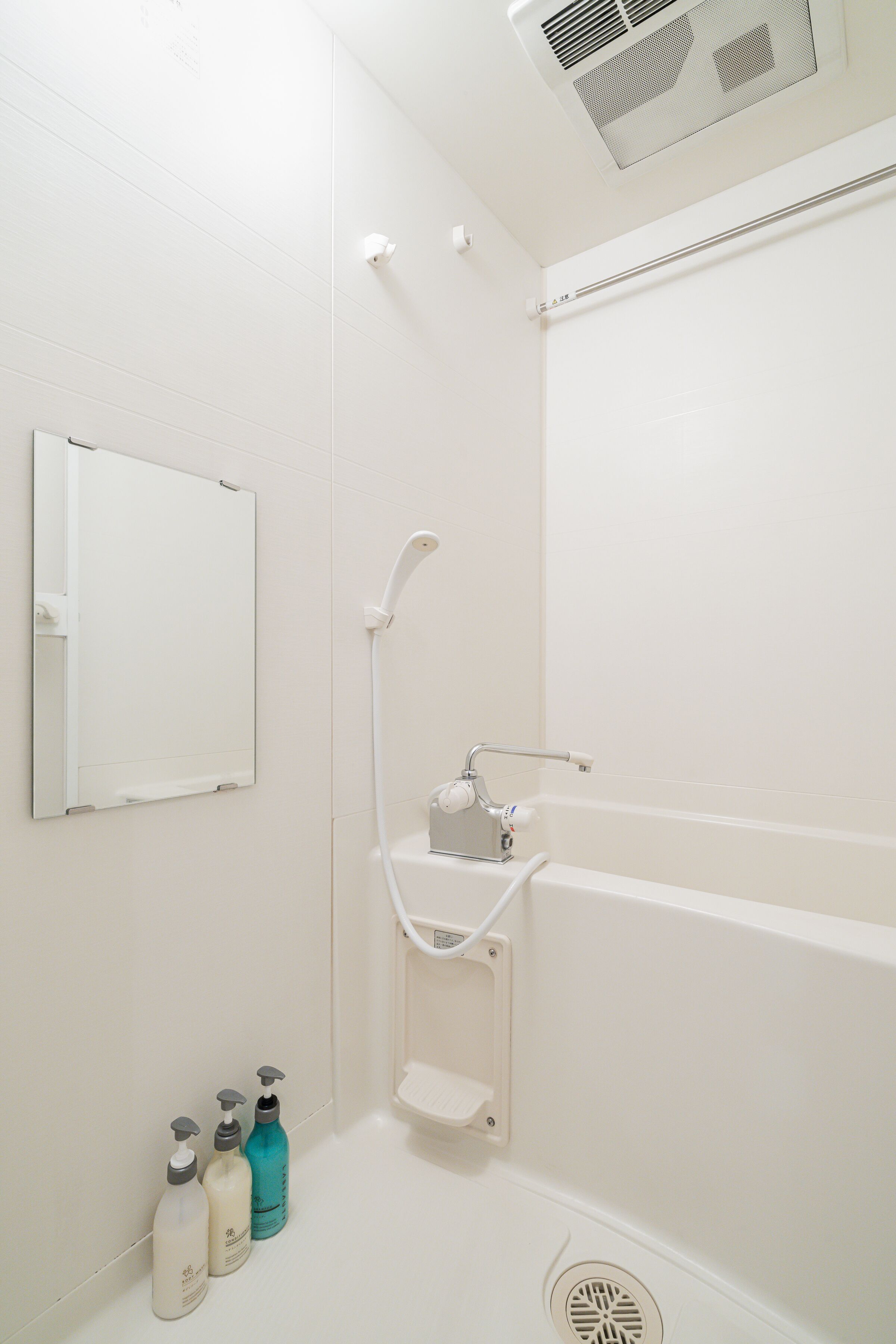 A white bathroom with a shower, a mirror, and a shelf with toiletries.