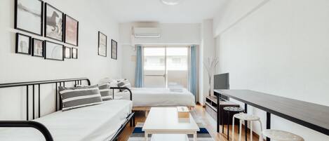 A modern hotel room with a bed, a small table, a TV, and a window with curtains.