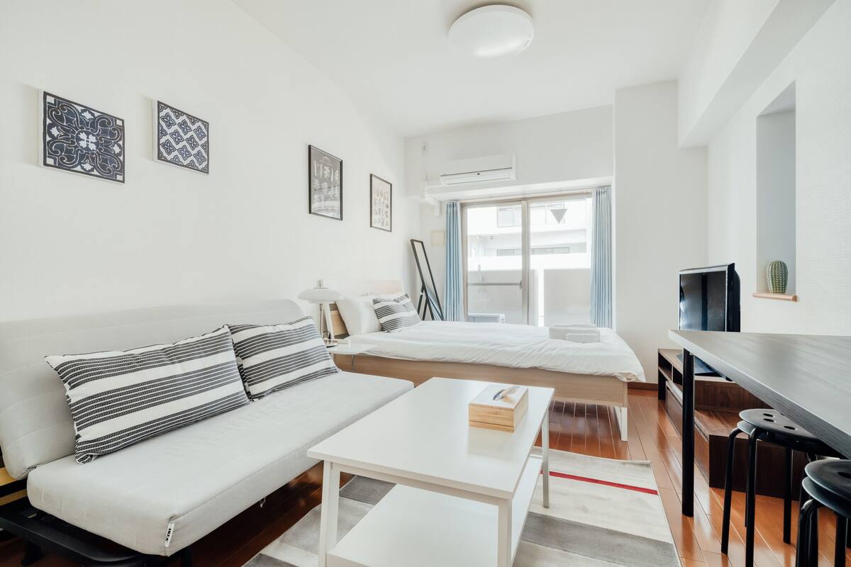 Quarto moderno e bem iluminado com sofá, cama, mesinha e televisão.