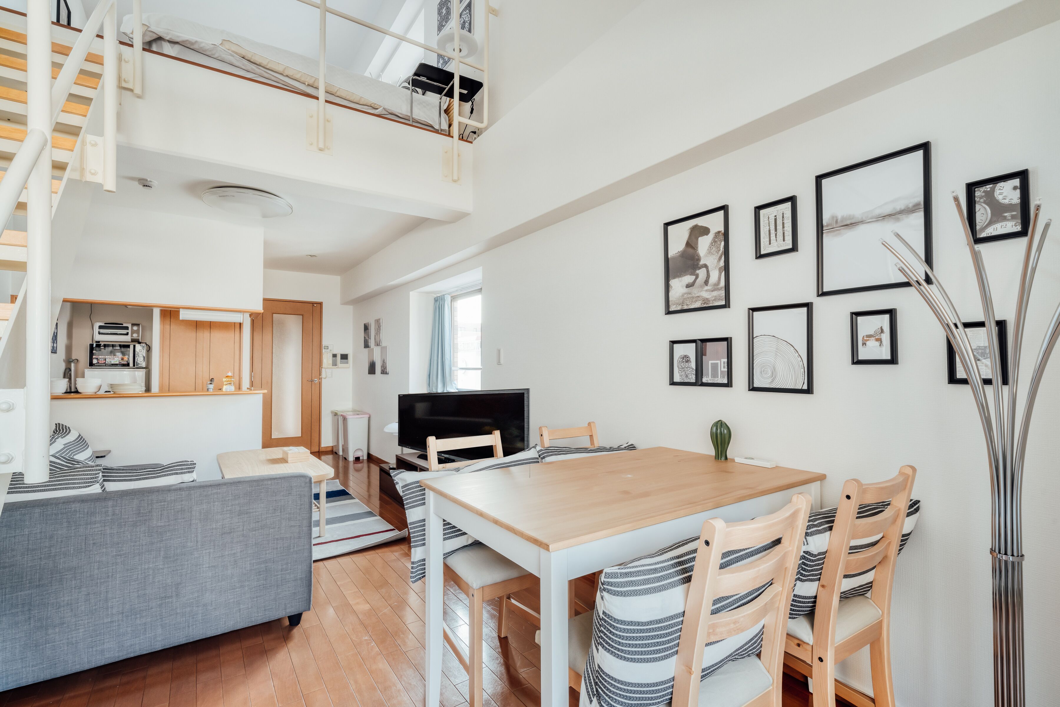 A modern living room with a wooden dining table, grey sofa, and a TV.