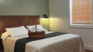 Un lit bien fait, avec une tête de lit, une lampe de chevet et une fenêtre équipée de stores.