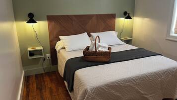 Een net opgemaakt bed met een houten hoofdbord, twee bedlampen, een klein plankje en een mandje op het bed.