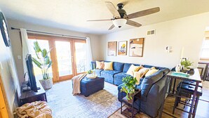 A living room with a blue sofa, a coffee table, a ceiling fan, and a dining area with a table and chairs.