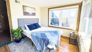 A bedroom with a bed, a potted plant, a window with a view, and a ceiling fan.