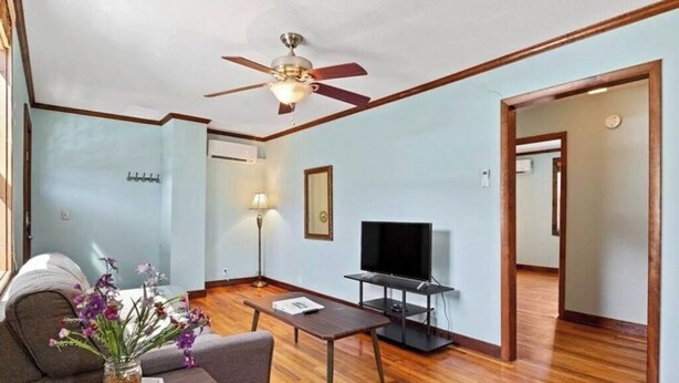 A living room with a ceiling fan, a flat-screen TV on a stand, a sofa, a coffee table, and a vase with flowers.