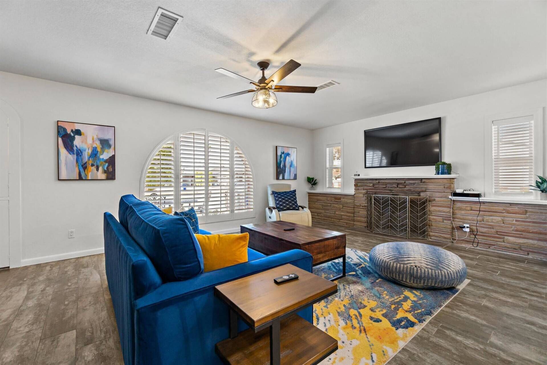 A modern living room with a blue sofa, a fireplace, a flat-screen TV, and a ceiling fan.