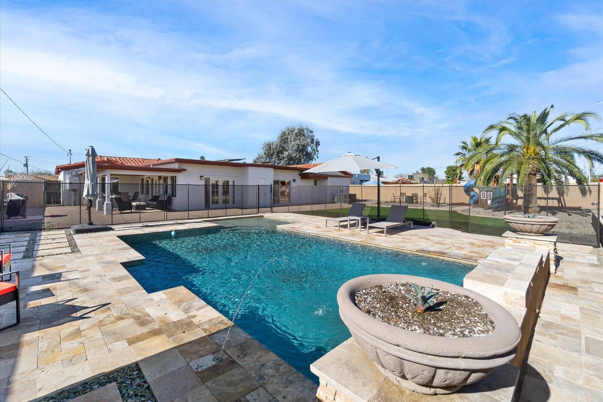 Une piscine avec une terrasse carrelée, un patio couvert et une maison en arrière-plan.