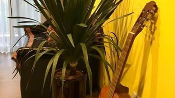 A room with a potted plant, a guitar, and a wooden floor.