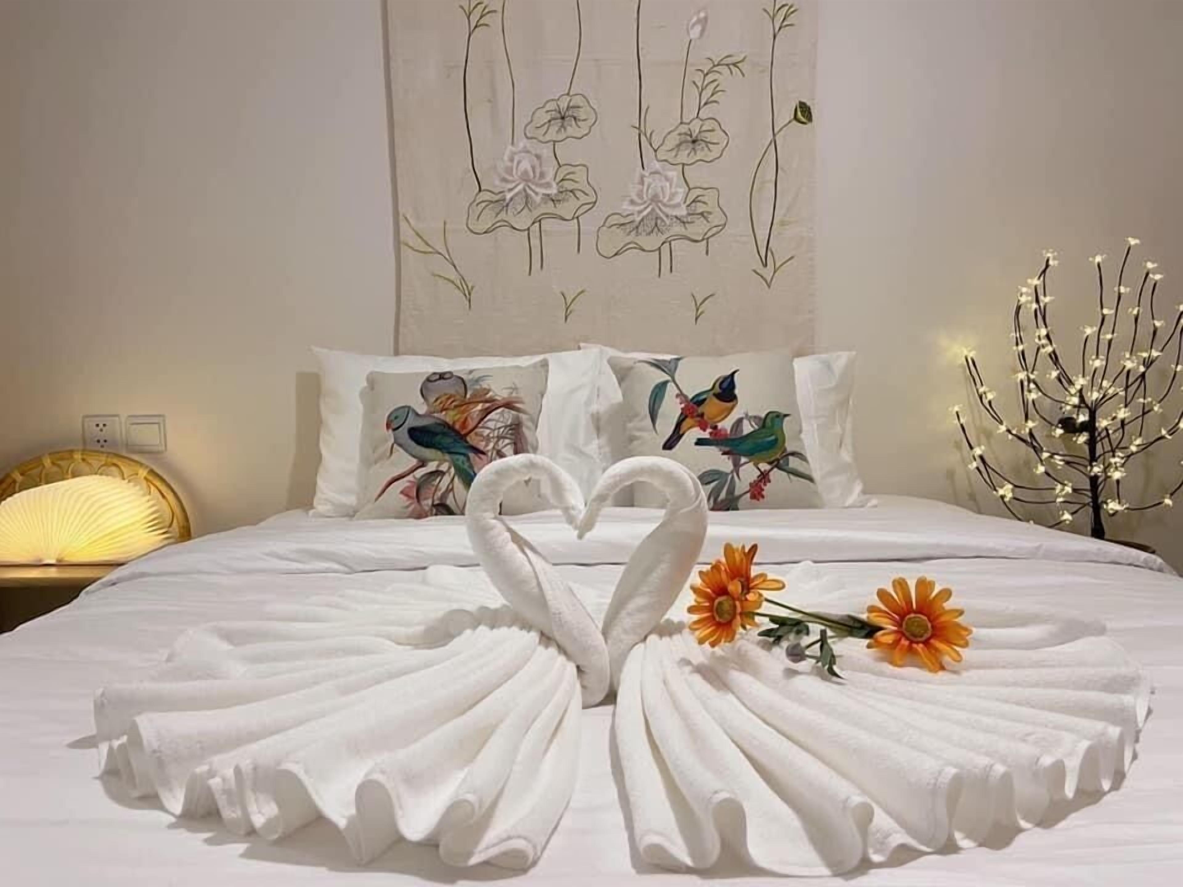 Una cama impecable con una toalla dispuesta en forma de corazón y dos flores.